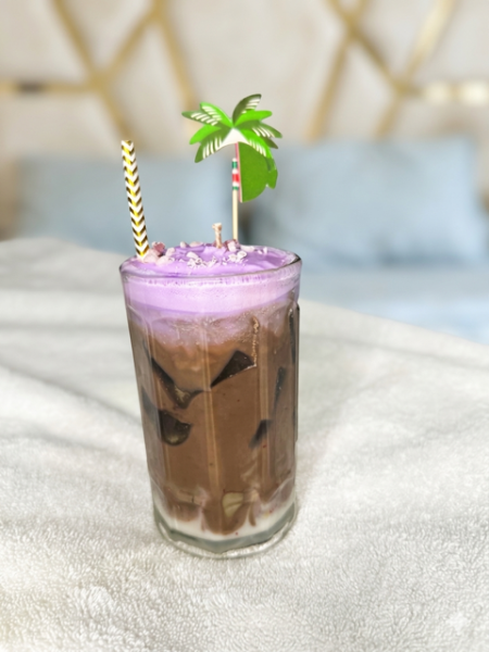 Glass of iced coffee with a purple top layer, palm tree straw, and decorative straw on a light surface.